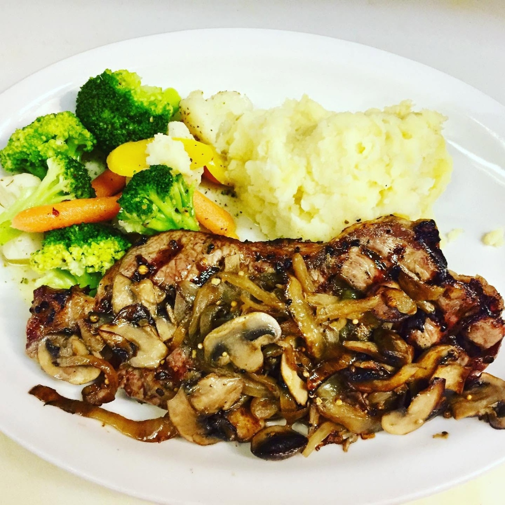 Pork chop smothered in sautéed mushrooms with mashed potatoes and steamed vegetables